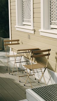 Simple outdoor setting with wooden chairs and table against a beige clapboard wall. Ideal for lifestyle or architecture.