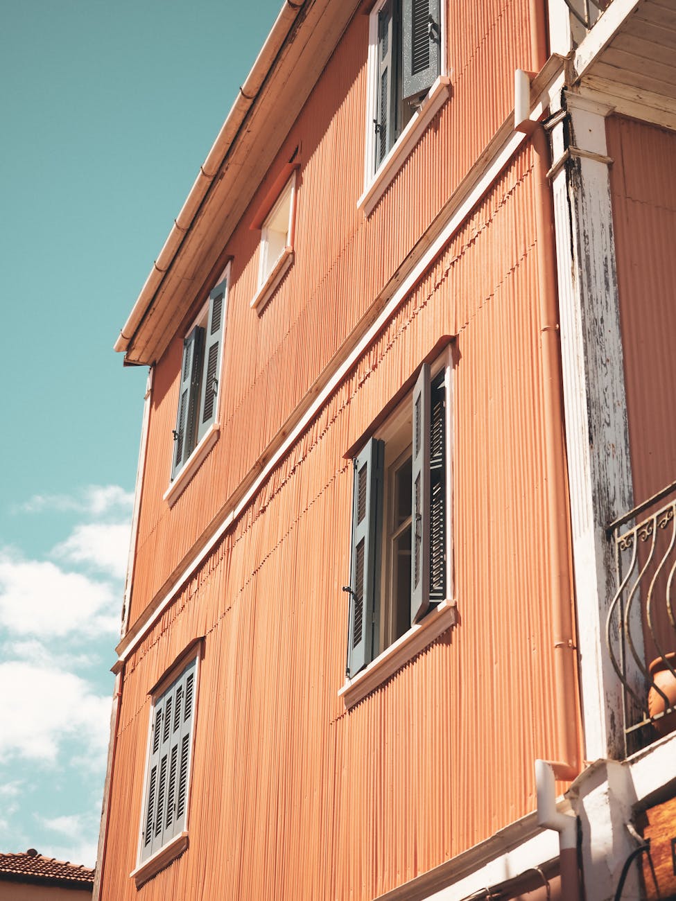 A vibrant orange house with open windows against a clear blue sky, highlighting architectural details.